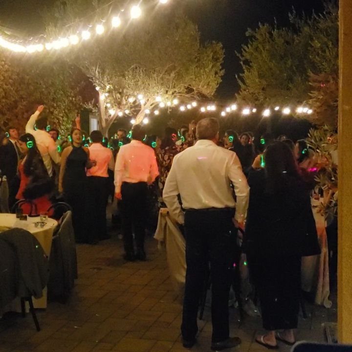 People dancing outdoors at night under festive strings of glowing lights.