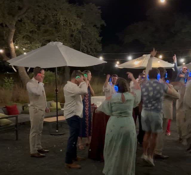 People dancing outdoors at night while wearing glowing blue wireless headphones for a silent disco.