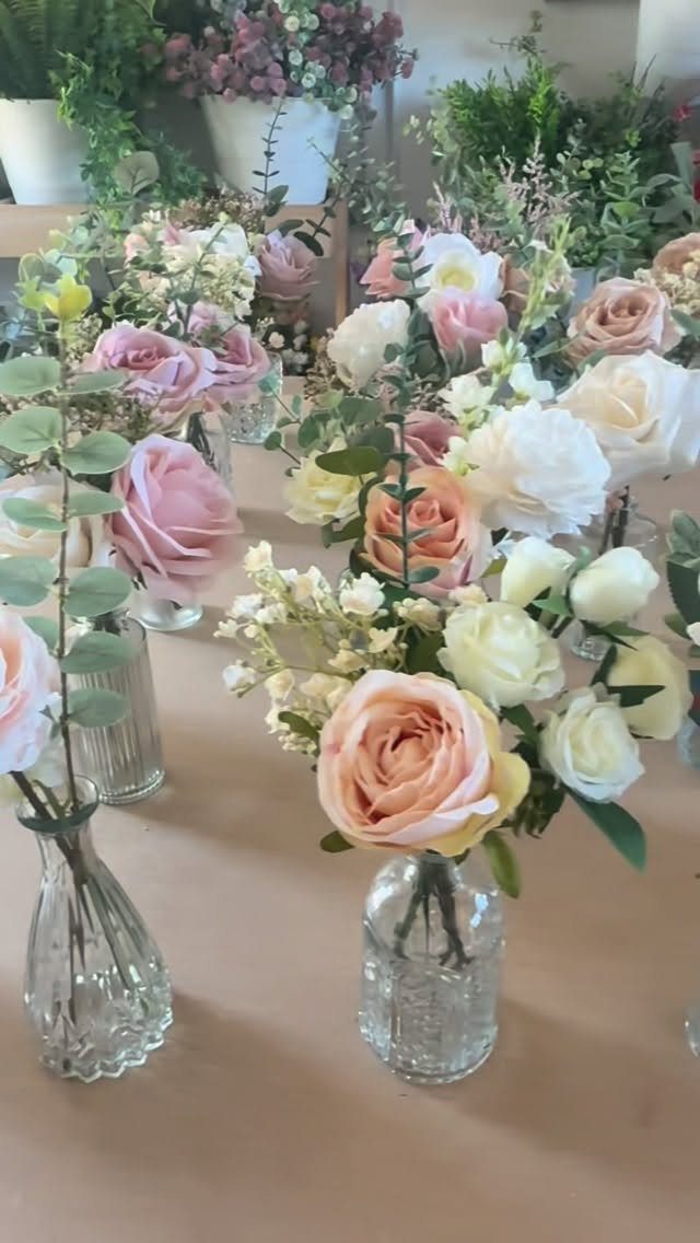 Small glass vases containing blush pink and cream roses with green eucalyptus leaves on a table.