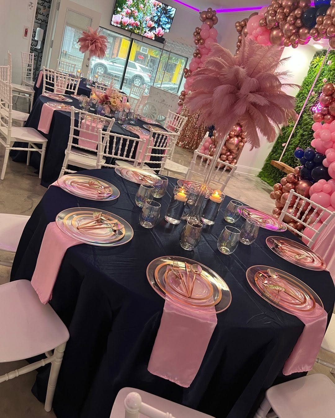 A navy blue tablecloth set with pink napkins, rose gold cutlery, and pink feather centerpieces.
