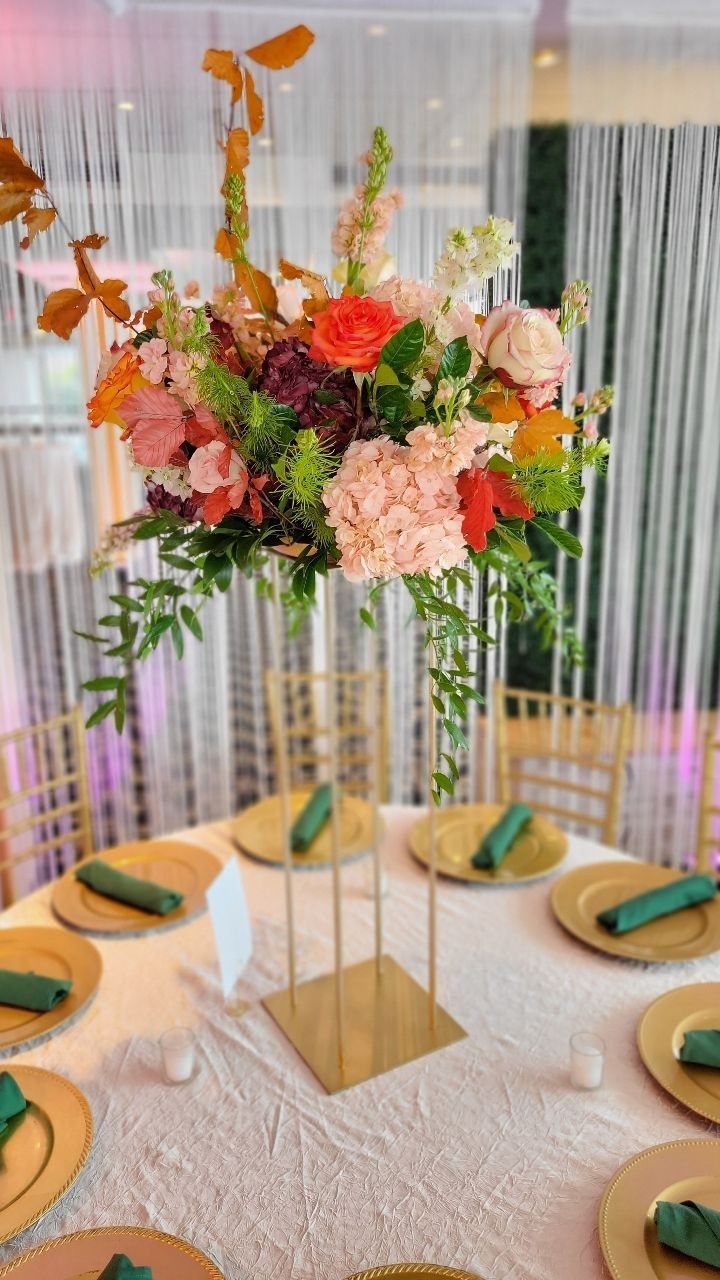 Floral centerpiece with pink and orange blooms on a gold stand at a decorated wedding table.