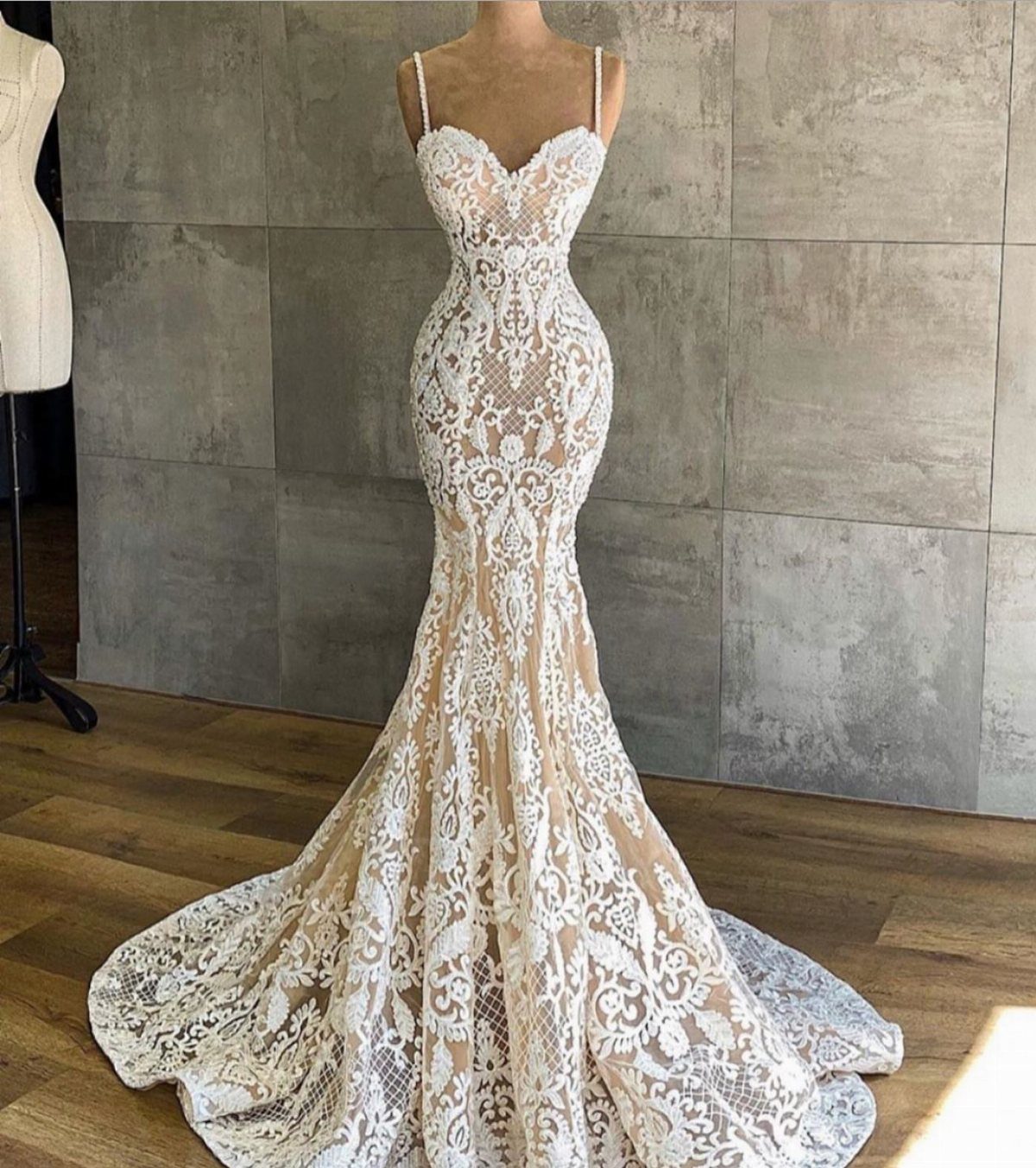 Intricate white lace mermaid wedding dress displayed on a mannequin in a studio setting.