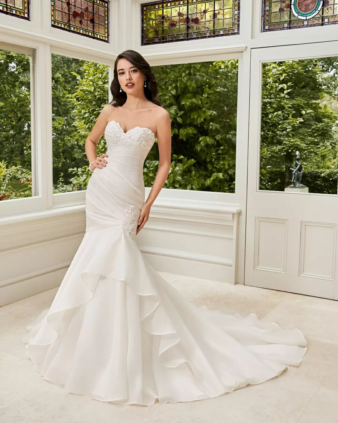 A woman wearing a white strapless wedding dress with a fitted bodice and flared ruffled skirt.