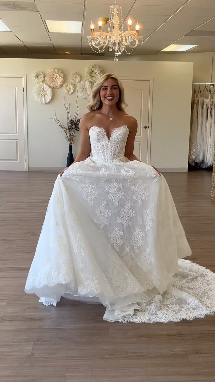 A smiling woman wearing a white lace wedding dress with a sweetheart neckline and full skirt.