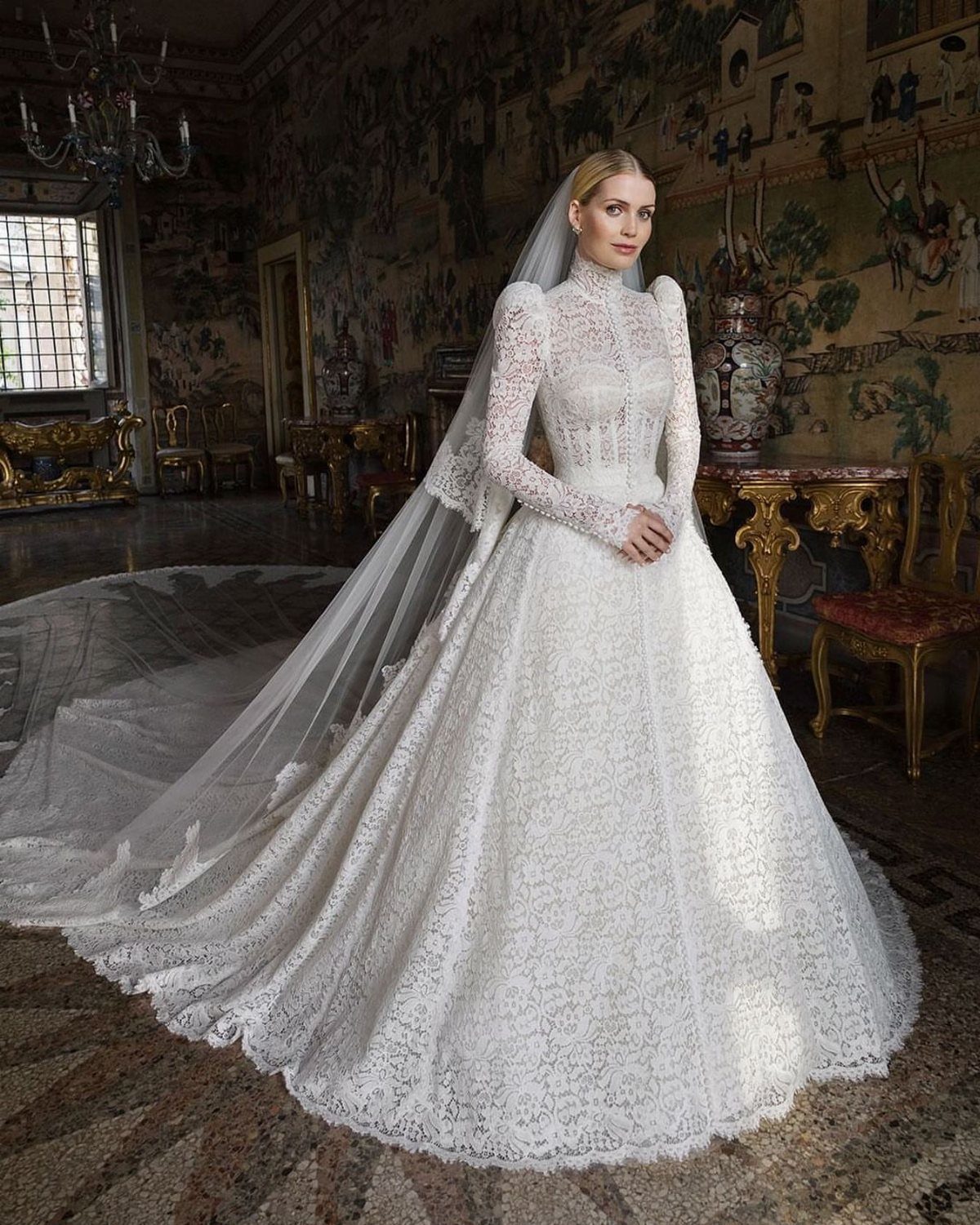 Woman in a white lace long sleeve wedding dress with a high neckline and long veil.