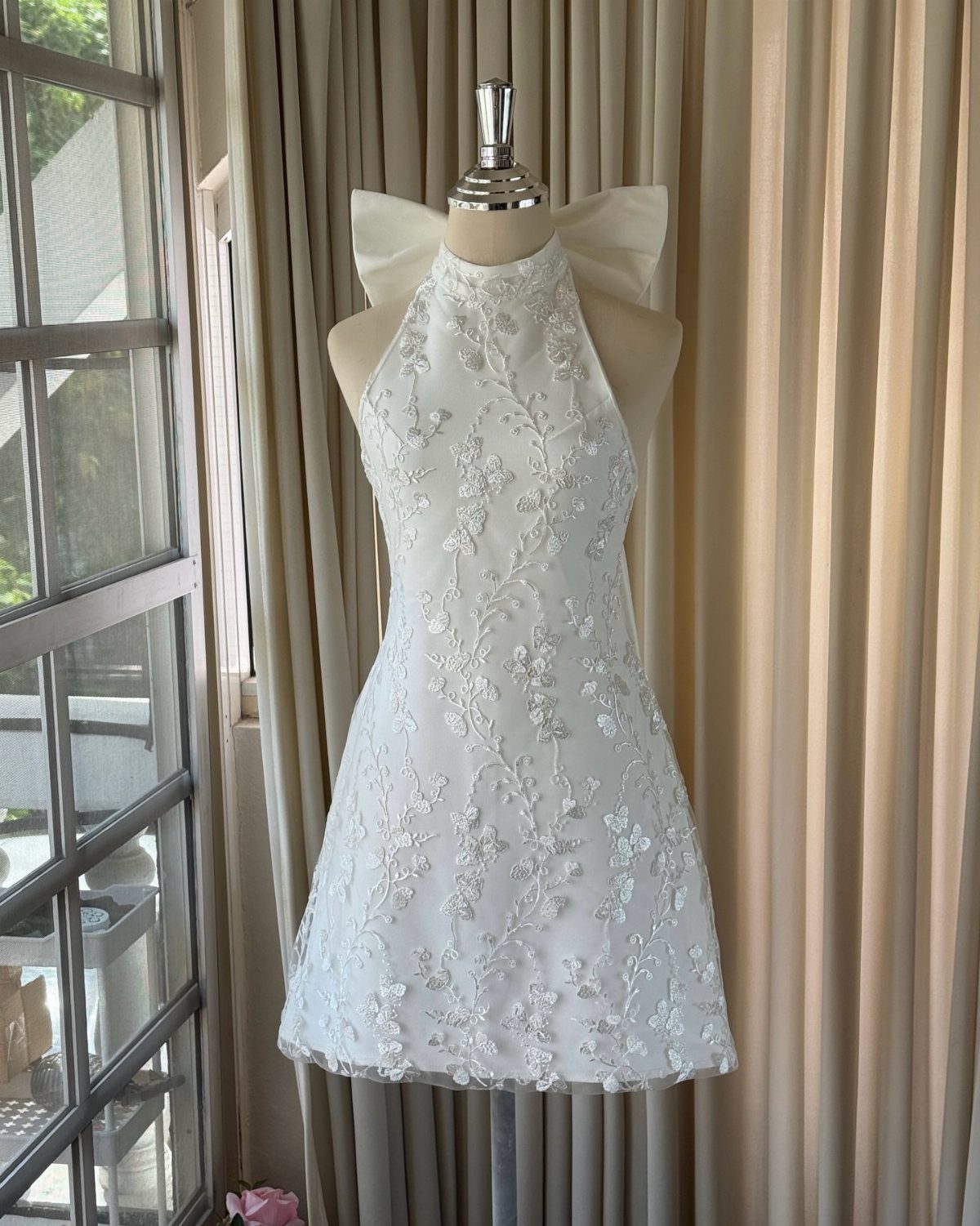 A short white floral lace wedding dress with a halter neck on a mannequin.