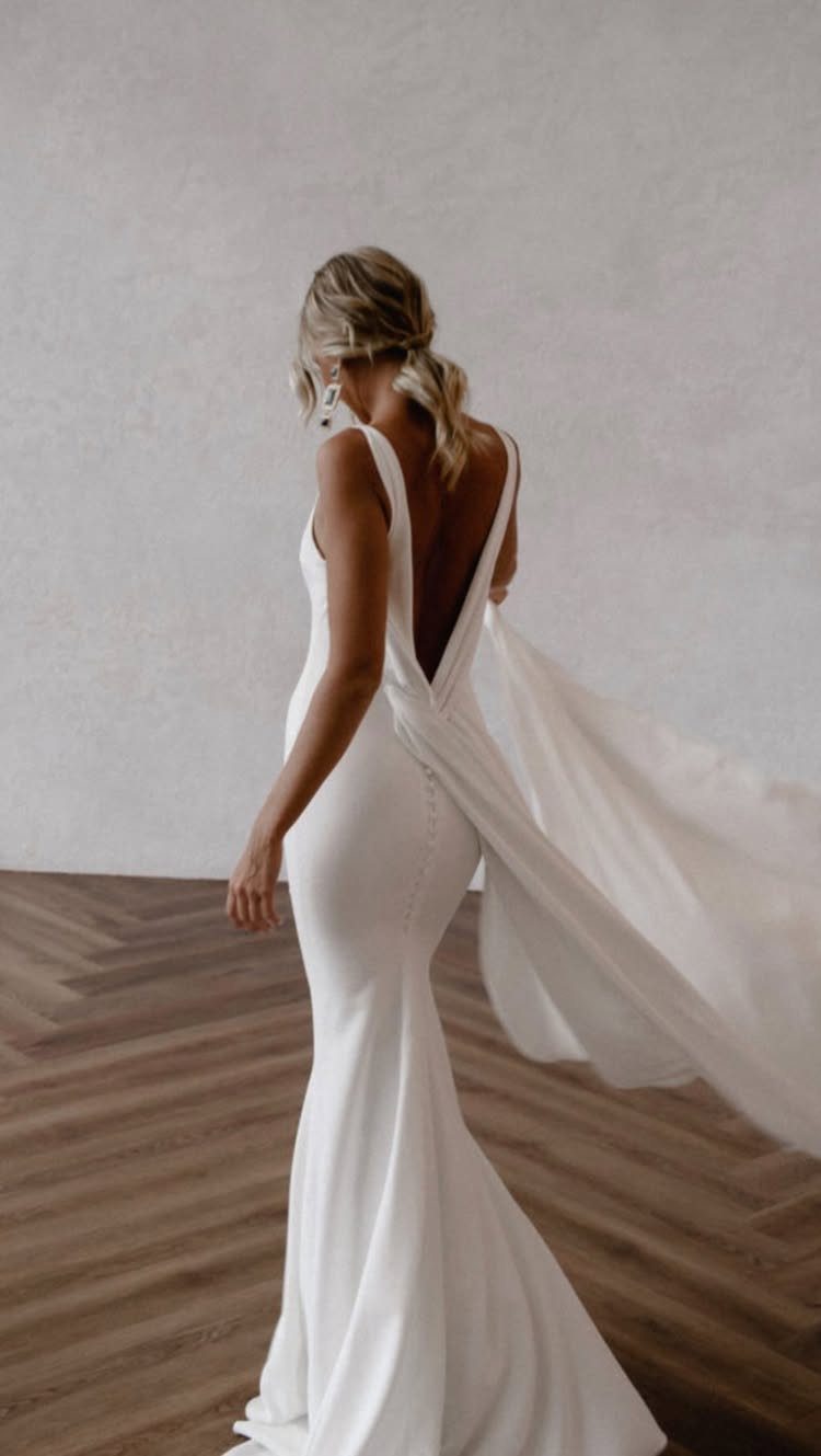 Woman in a sleek white minimalist wedding dress with a deep V-neckline and flowing train.