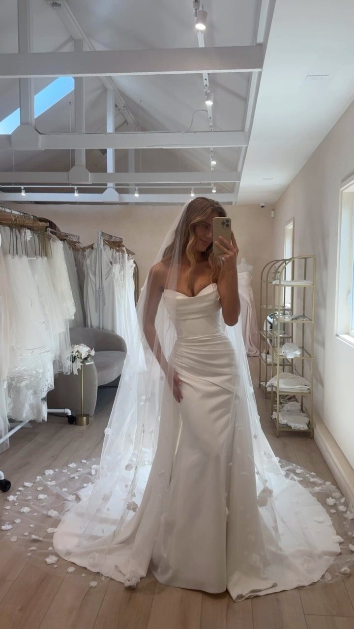 A woman wearing a white strapless wedding dress with a long veil in a bridal shop.