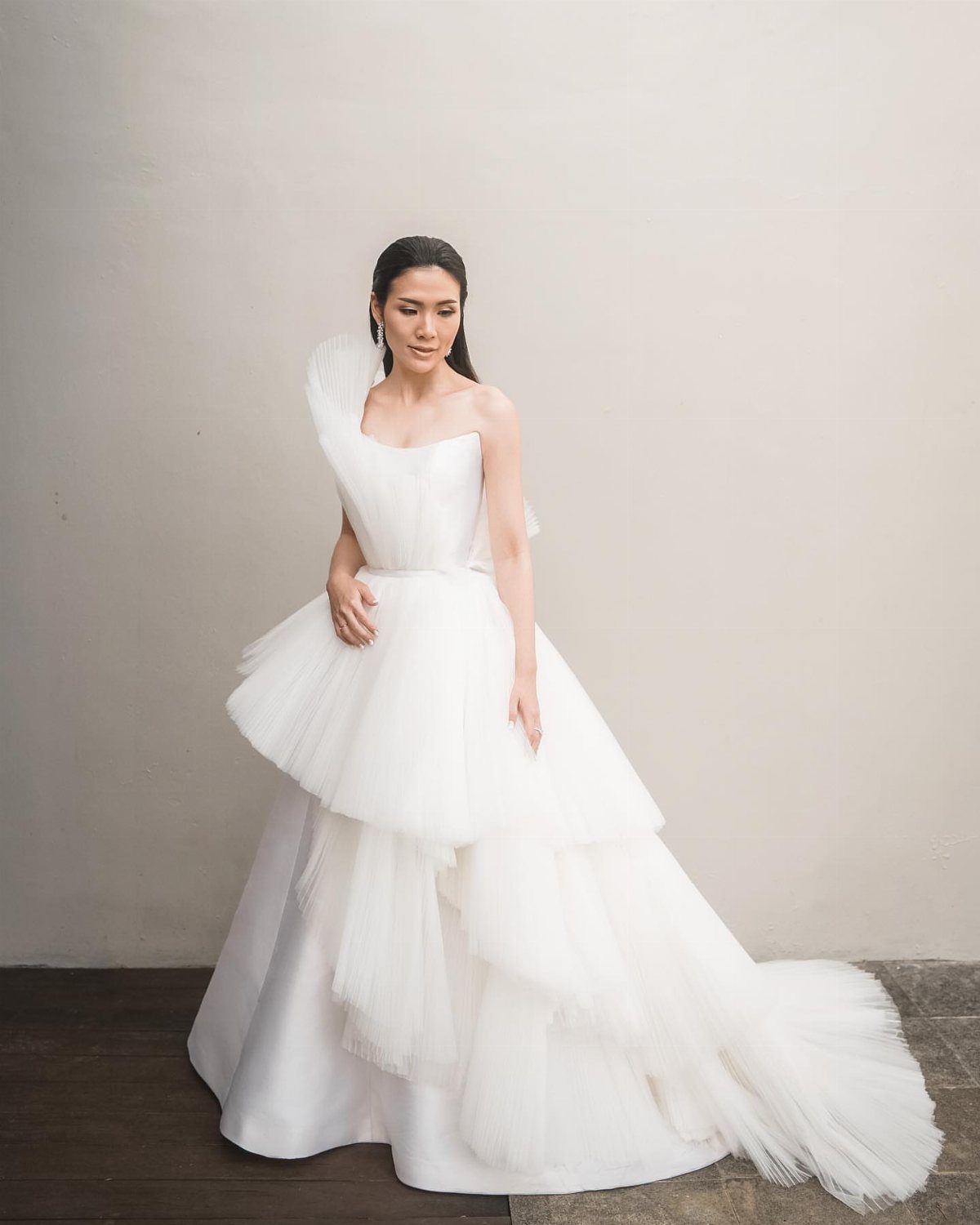 Woman in a white one-shoulder wedding dress with a voluminous tiered tulle skirt.