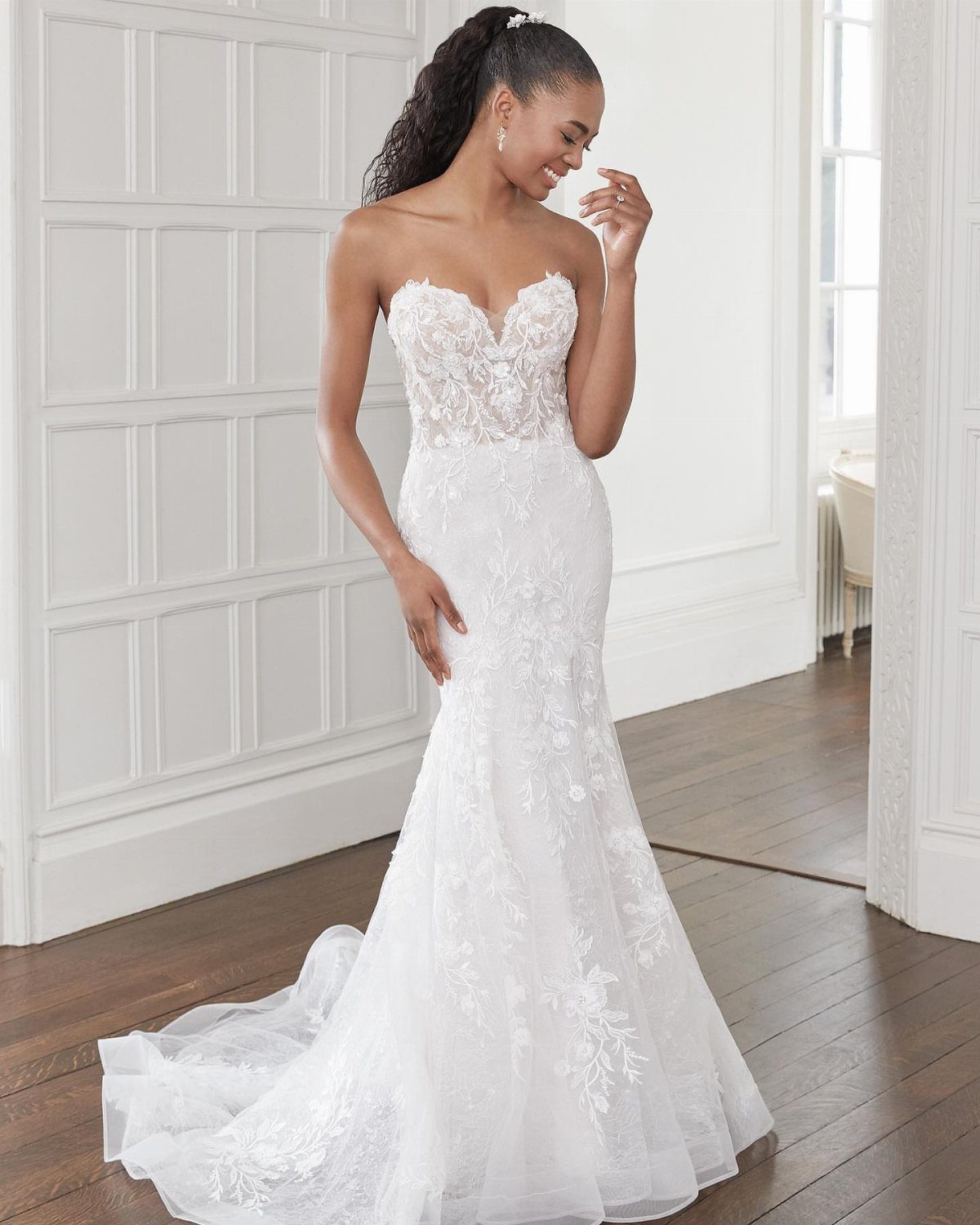A woman posing in a white lace strapless wedding dress with a flared trumpet silhouette.