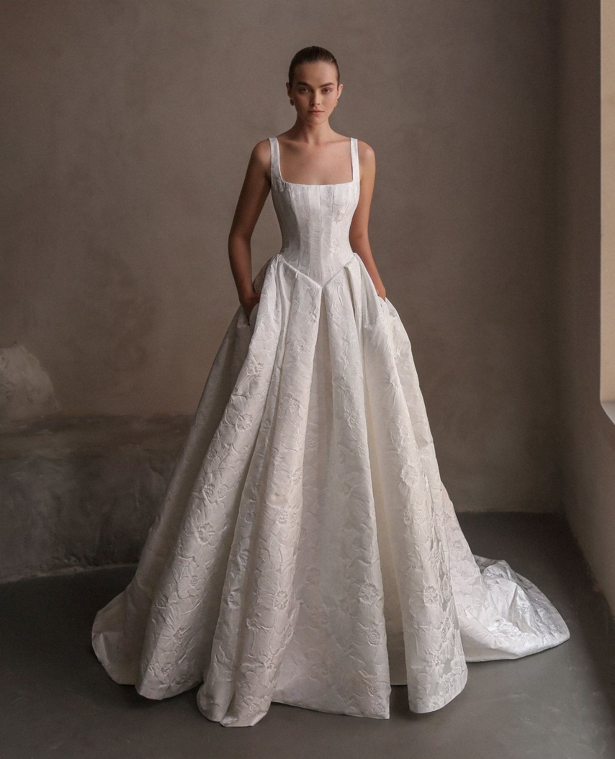 Woman in a white textured wedding gown featuring a square neckline and basque waistline.