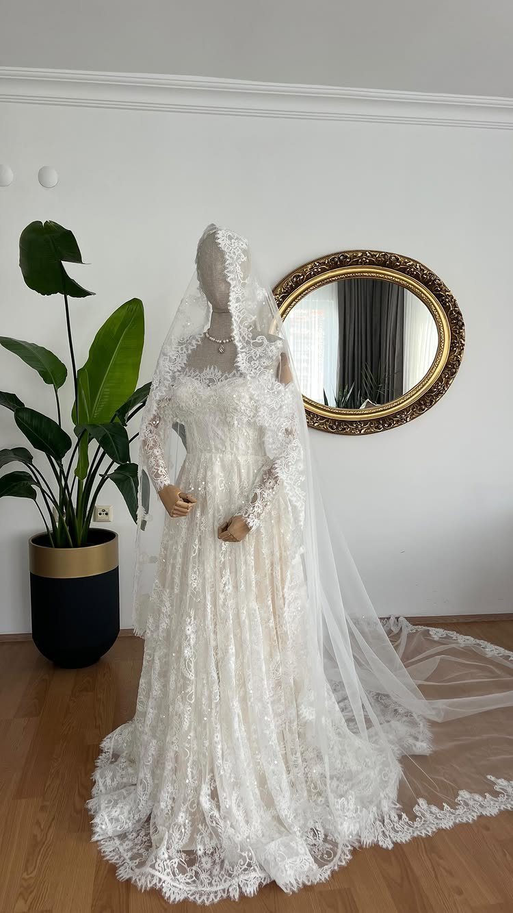 A white lace wedding gown with long sleeves and a veil displayed on a mannequin.