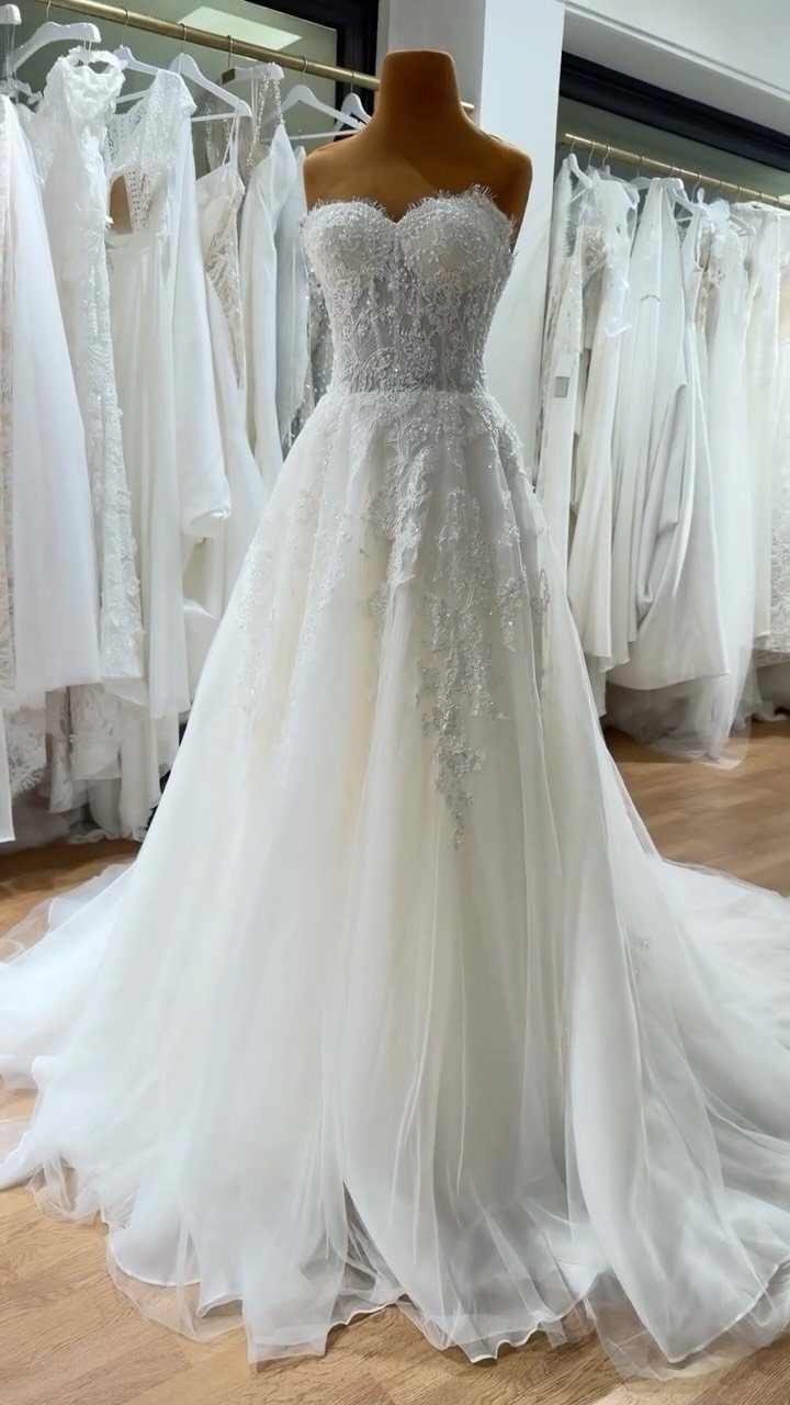 A white lace wedding dress with a voluminous tulle skirt displayed on a mannequin.