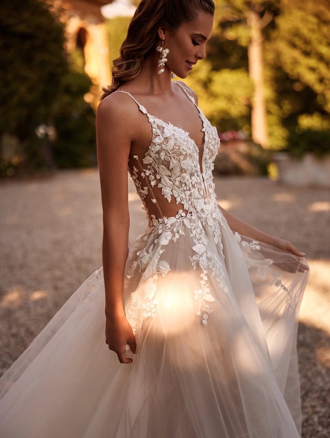 Woman in a white lace wedding dress with modern side cut-outs standing in a garden.