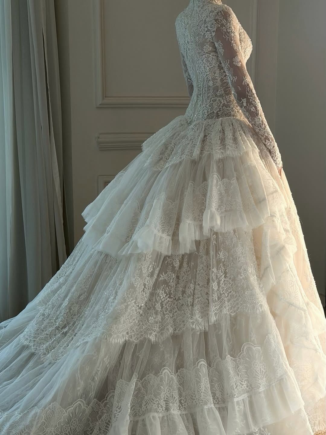 A lace wedding dress with long sleeves and a voluminous tiered tulle skirt.