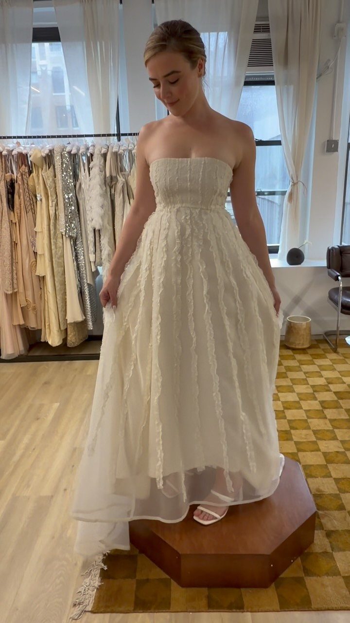 Woman wearing a strapless white empire-waist wedding dress standing on a wooden platform.