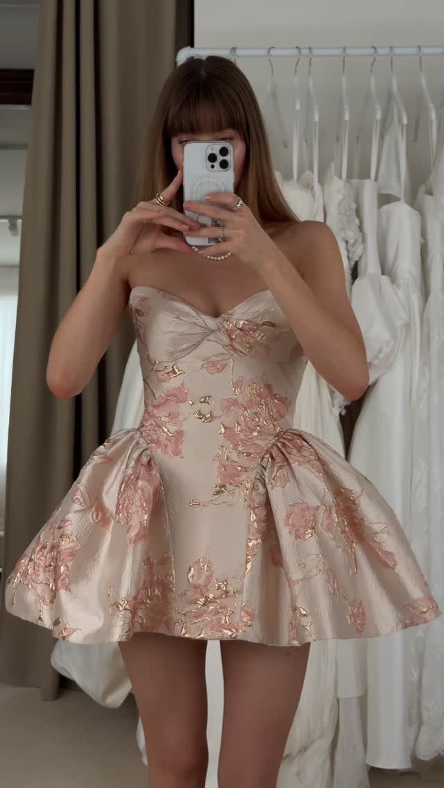 Woman in a strapless champagne floral mini dress taking a mirror selfie.