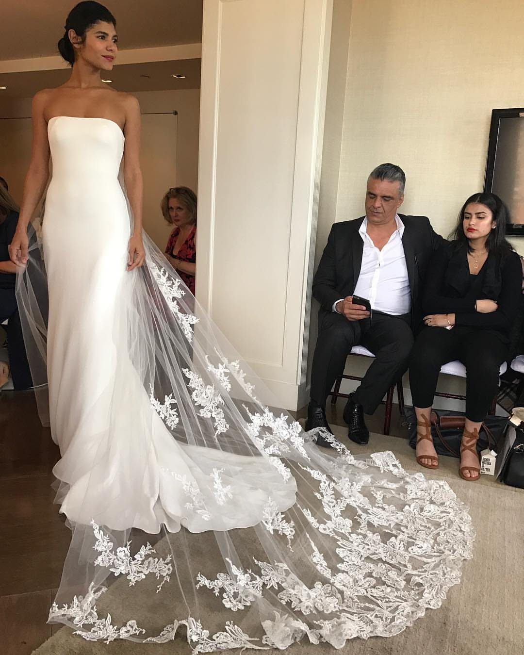 Woman wearing a white strapless sheath wedding dress with a long lace veil.
