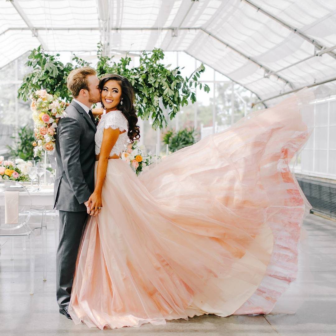 Bride in a white lace crop top and peach tulle skirt posing with a groom.