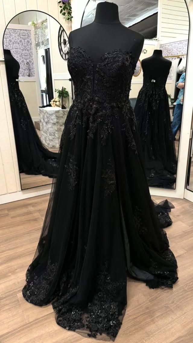 Black strapless wedding dress with lace floral embroidery displayed on a mannequin in a boutique.