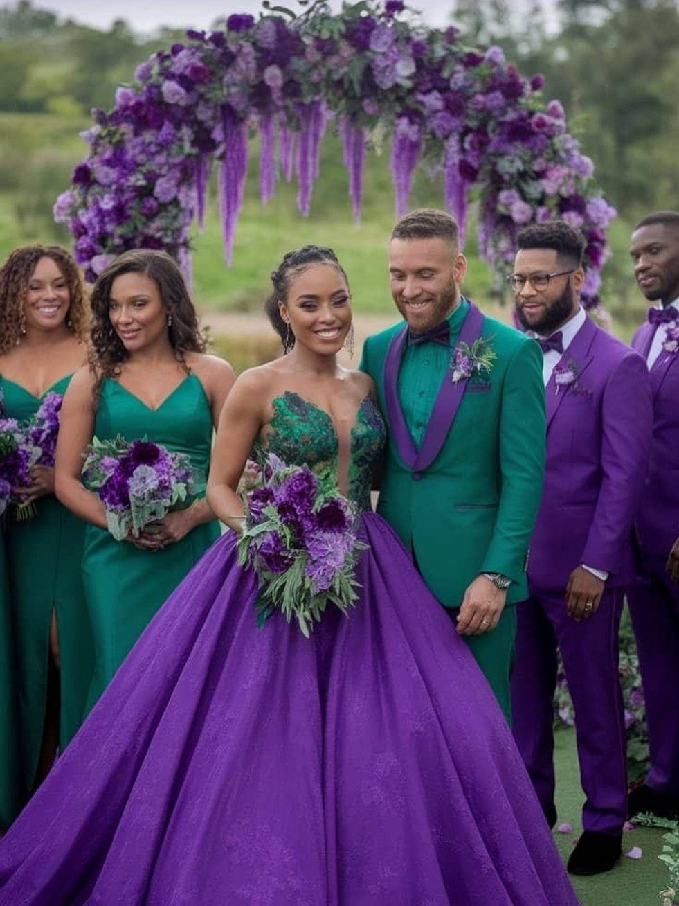 A bride in a purple ballgown and green bodice stands with her wedding party.