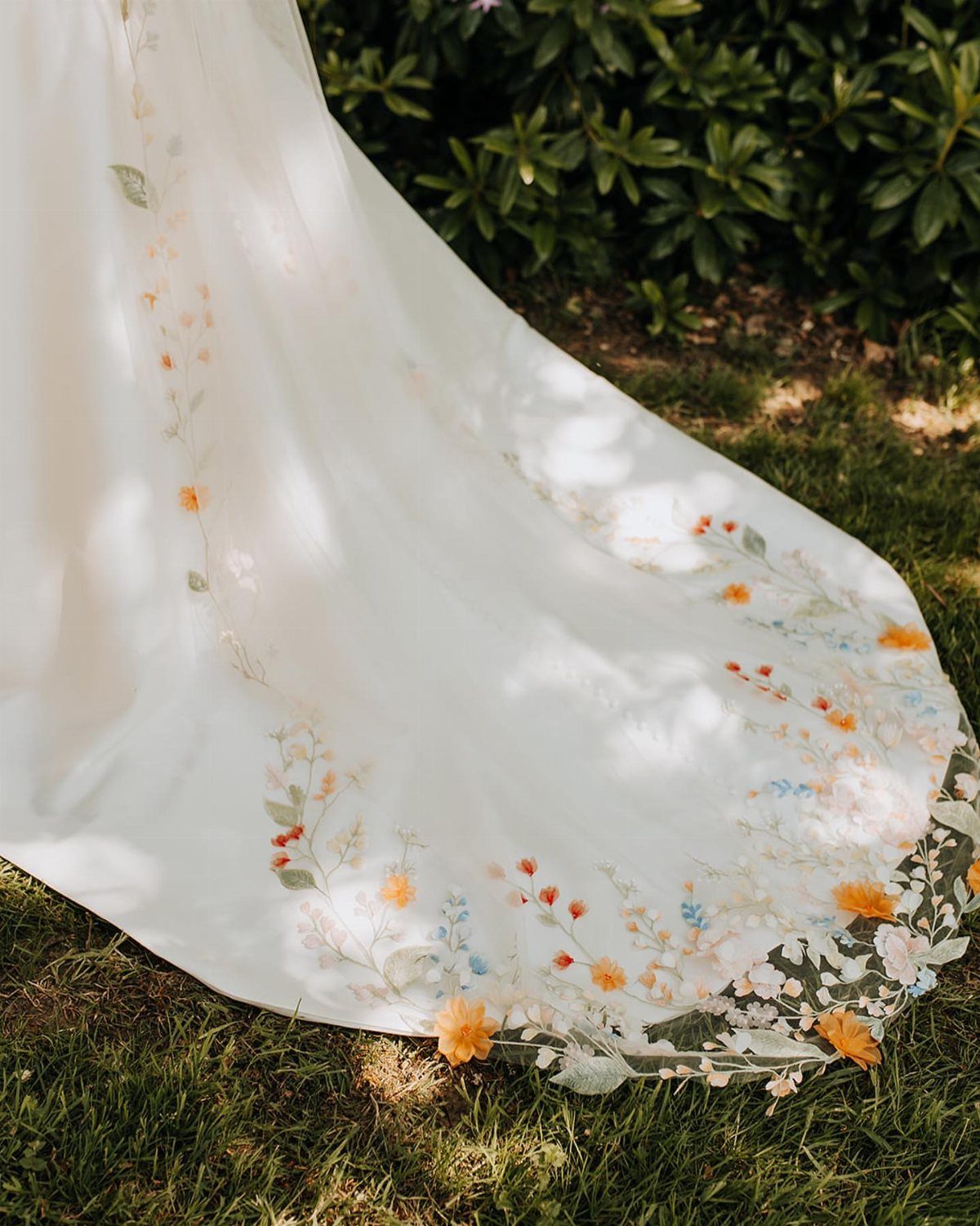 White wedding dress train with colorful embroidered floral patterns resting on green grass.