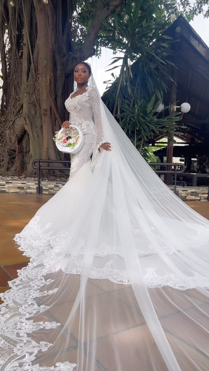 Woman in a white lace wedding dress wearing a long cathedral veil outdoors.