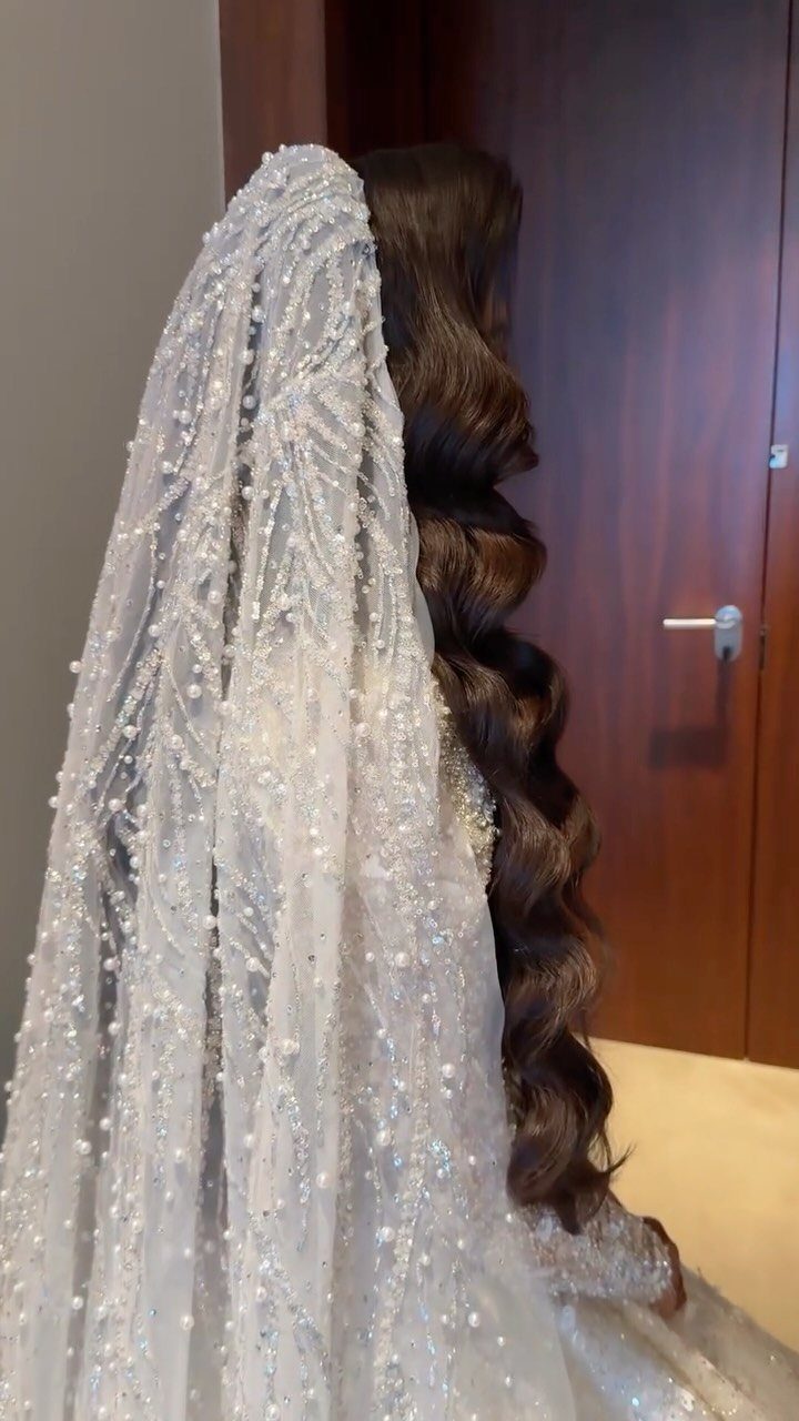 Long wavy dark hair styled with a pearl-embellished white wedding veil.