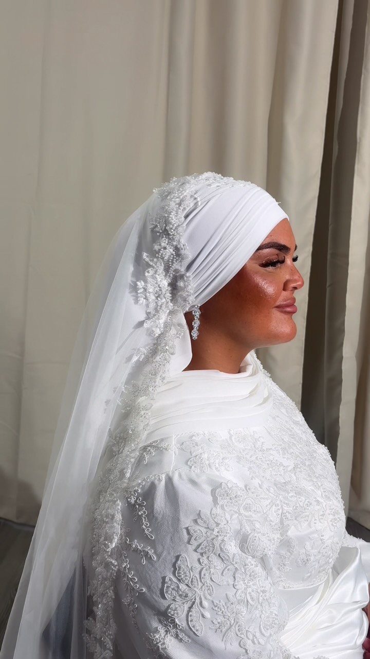 Woman in profile wearing an embroidered white wedding dress and a lace-edged veil.
