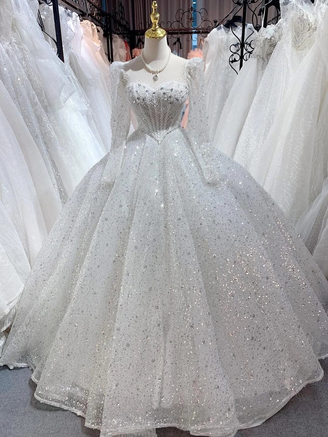 A shimmering white ballgown wedding dress with long sleeves displayed on a mannequin.
