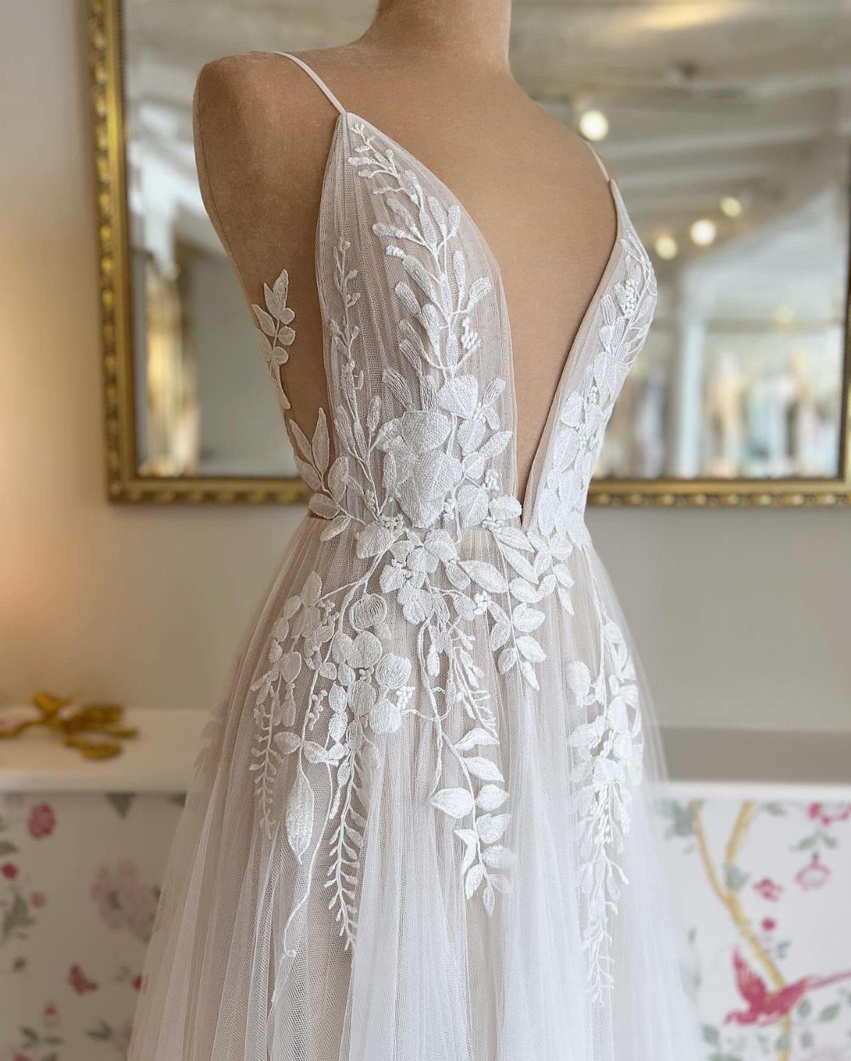 White lace wedding dress with floral appliqués and thin straps displayed on a mannequin.