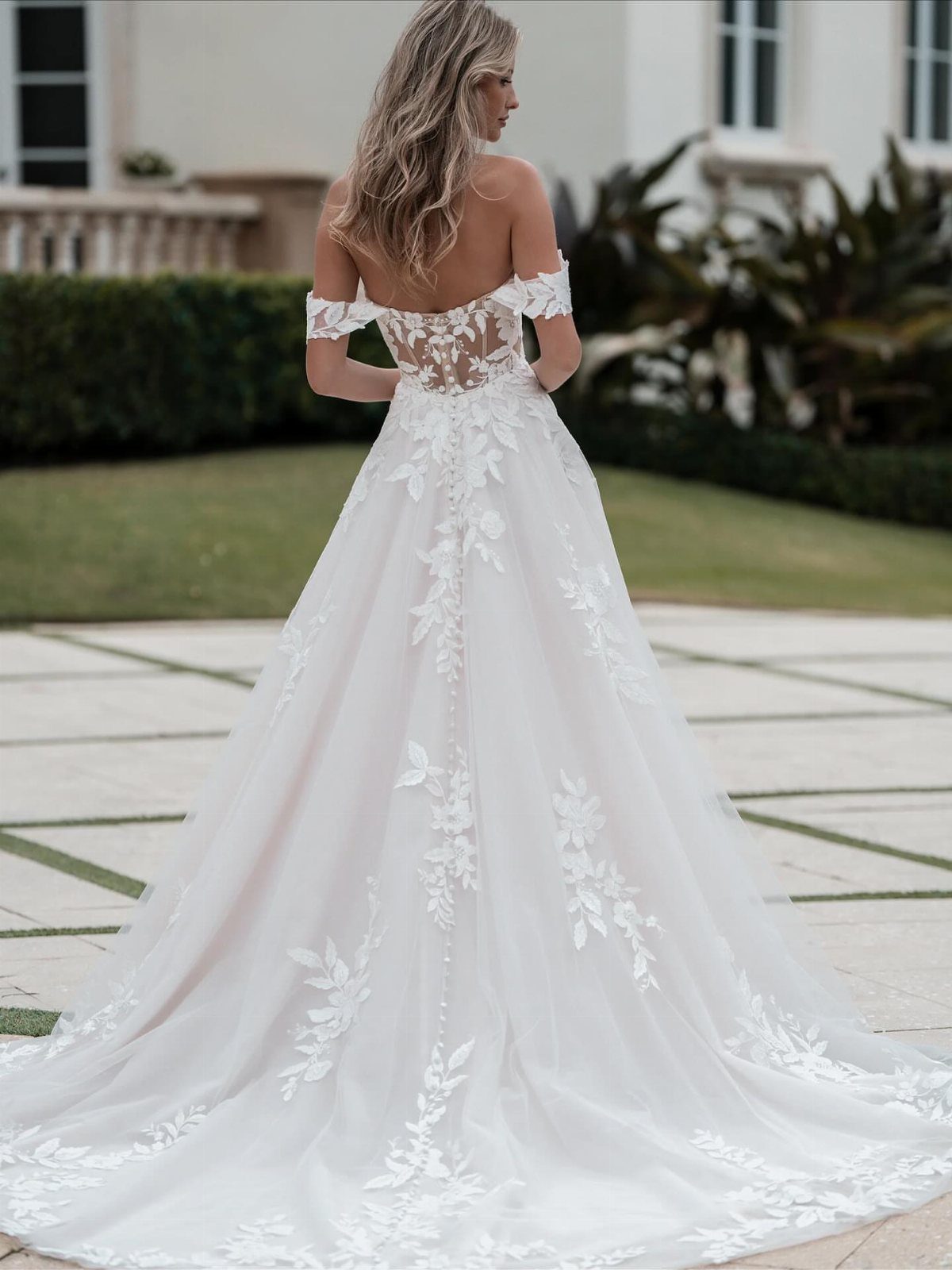 Woman in an off-the-shoulder white lace A-line wedding dress with a long train.