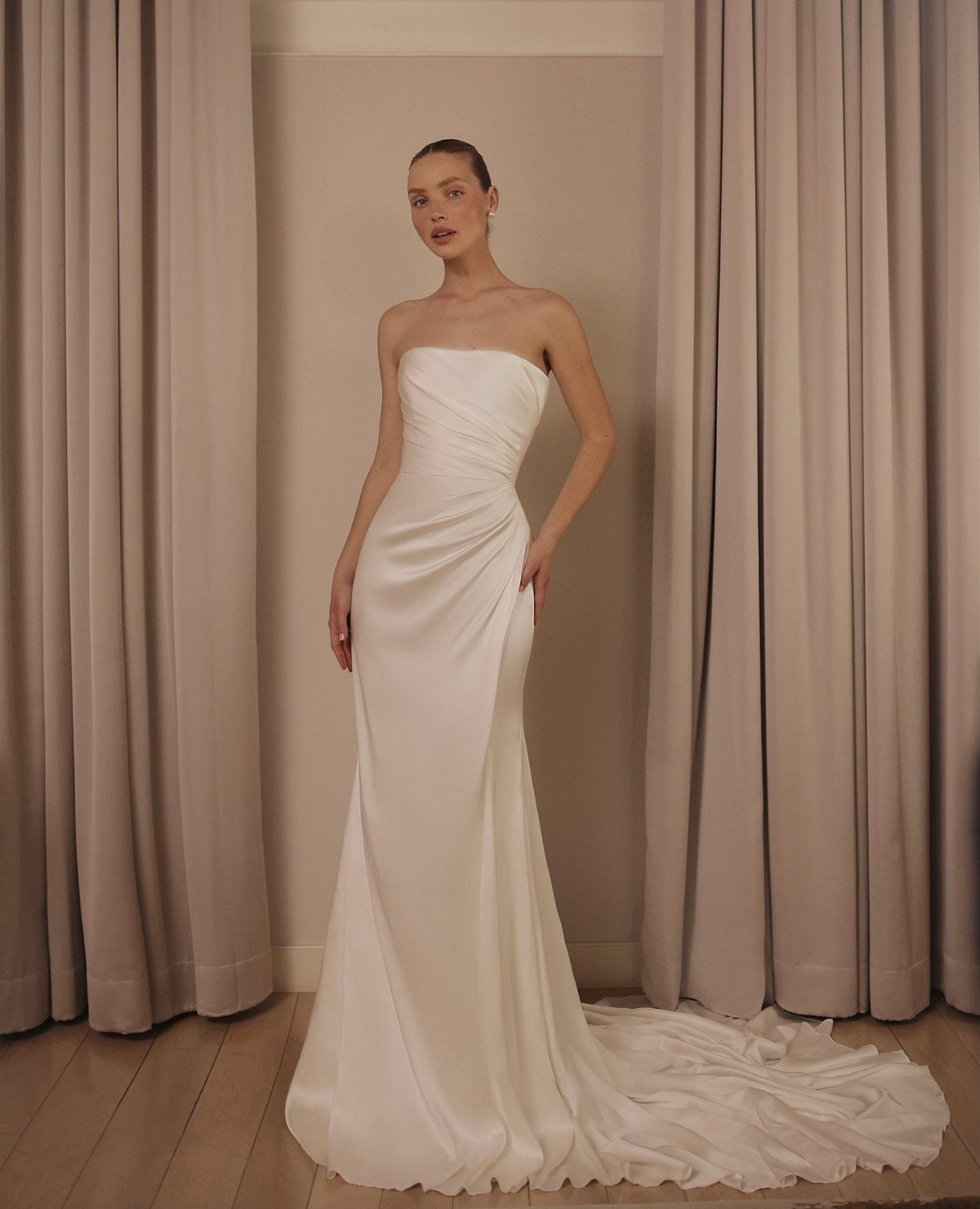 Woman wearing a strapless white minimalist sheath wedding dress standing between neutral curtains.