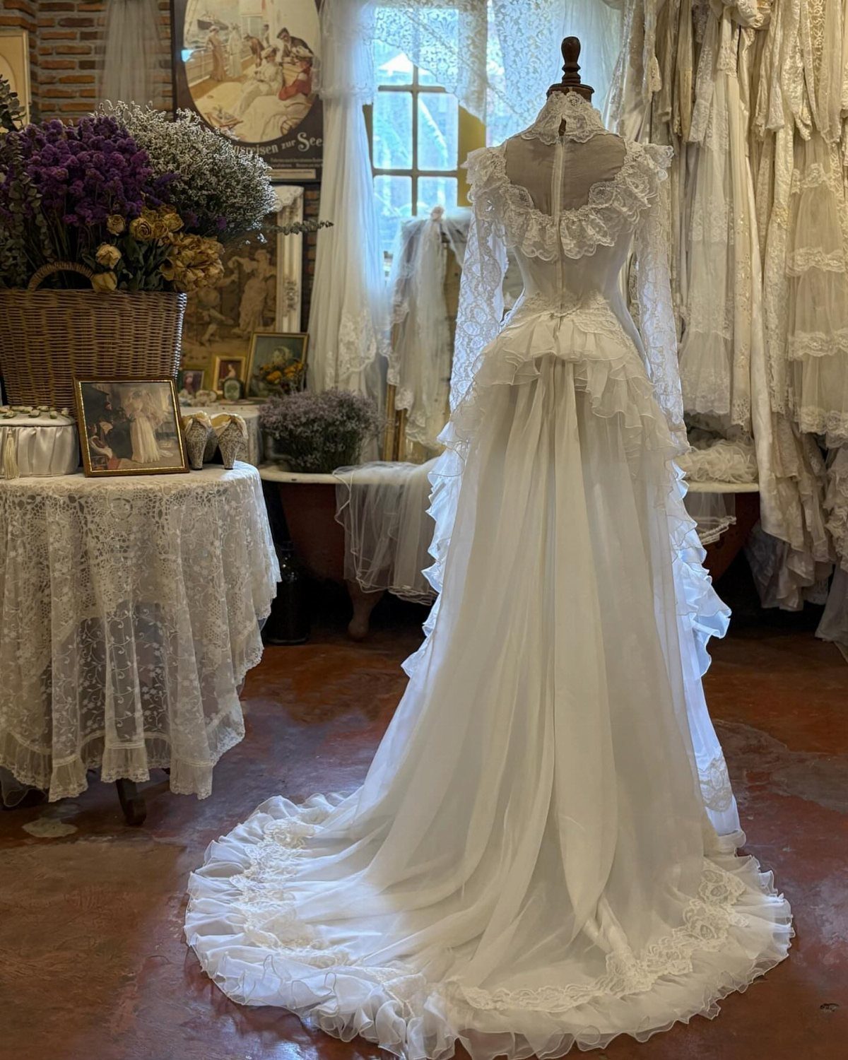 A white lace wedding dress with long sleeves and ruffles displayed on a mannequin.