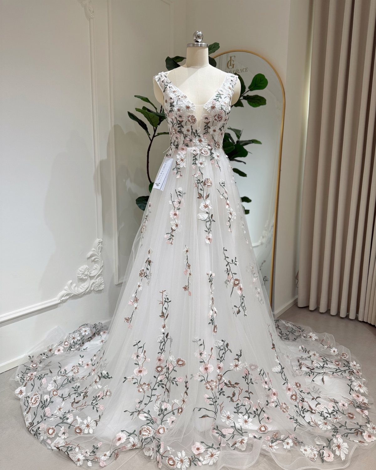 White wedding dress with pink floral appliques displayed on a mannequin with a long train.