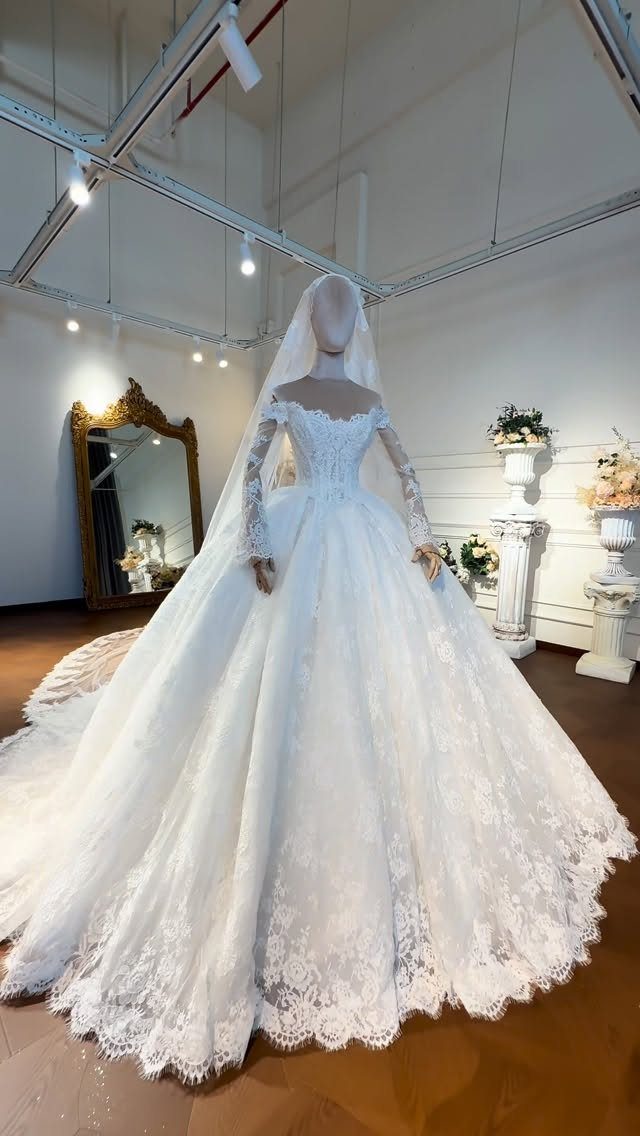 White lace wedding dress with long sleeves and a voluminous ball gown skirt on a mannequin.