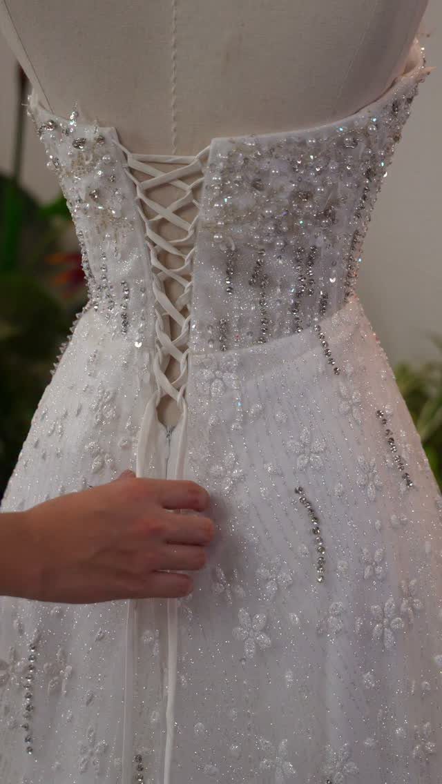 White beaded wedding dress with a lace-up corset back being adjusted by a hand.