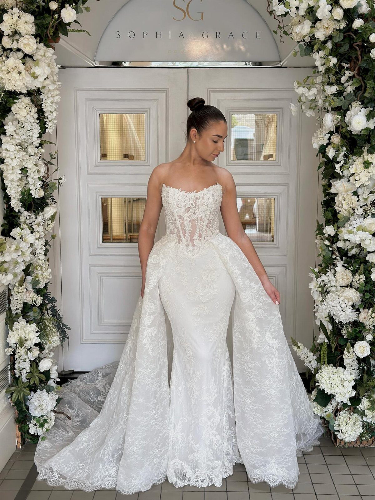 Woman wearing a white lace mermaid wedding dress with a large detachable lace overskirt.