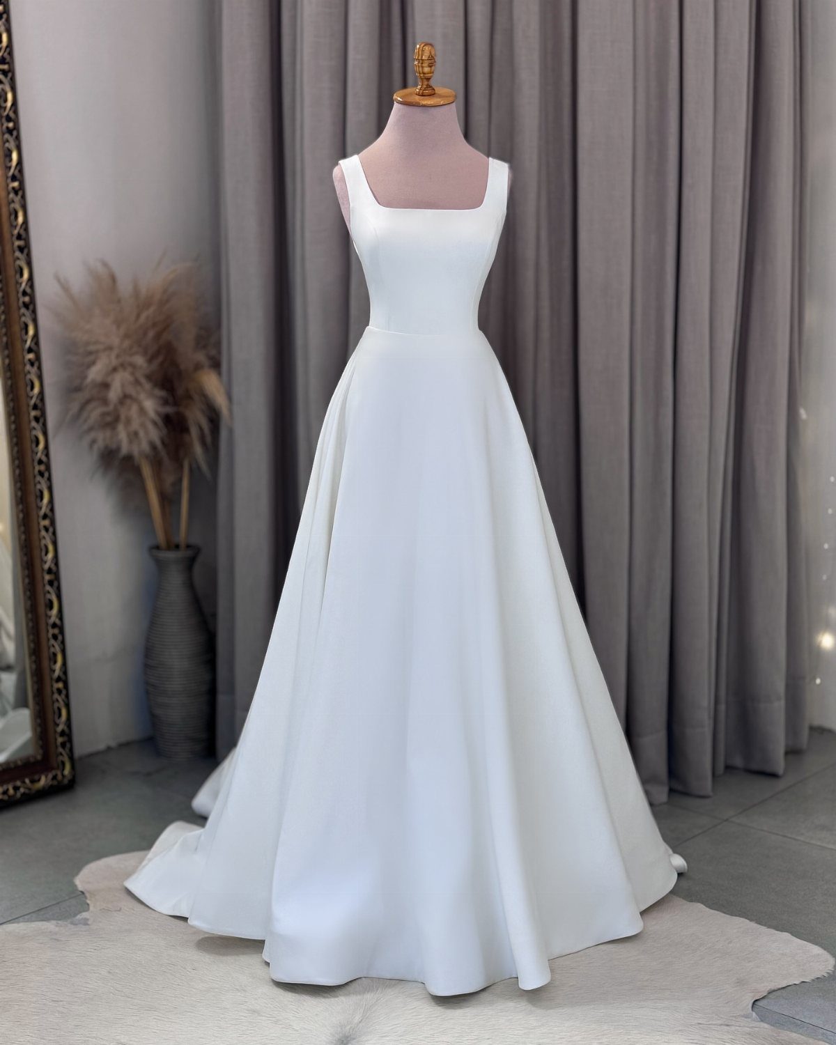 A sleek white satin wedding dress with a square neckline displayed on a mannequin.