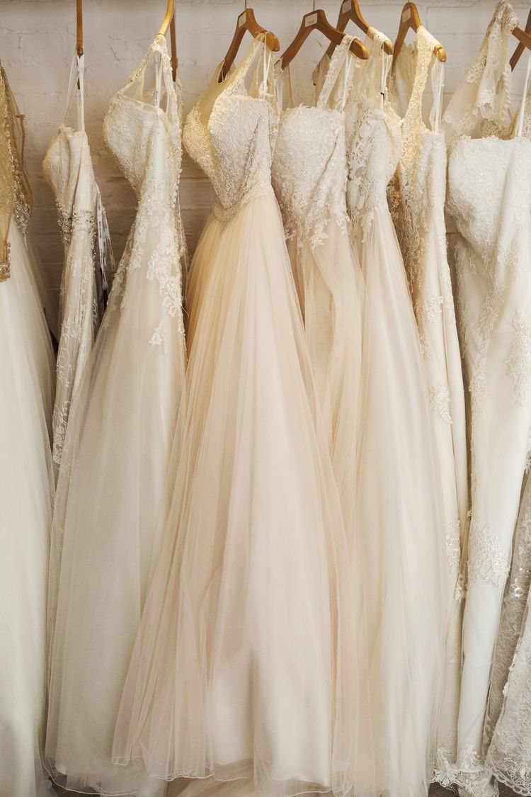 White and ivory wedding dresses hanging on wooden hangers in a bridal shop.