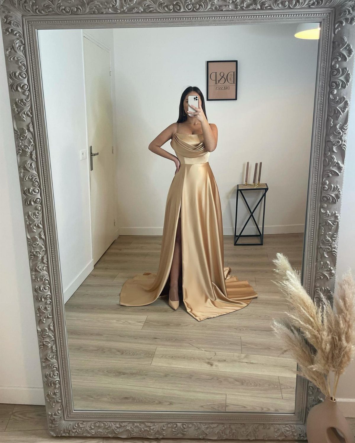 Woman in a long gold metallic satin gown posing for a mirror selfie.