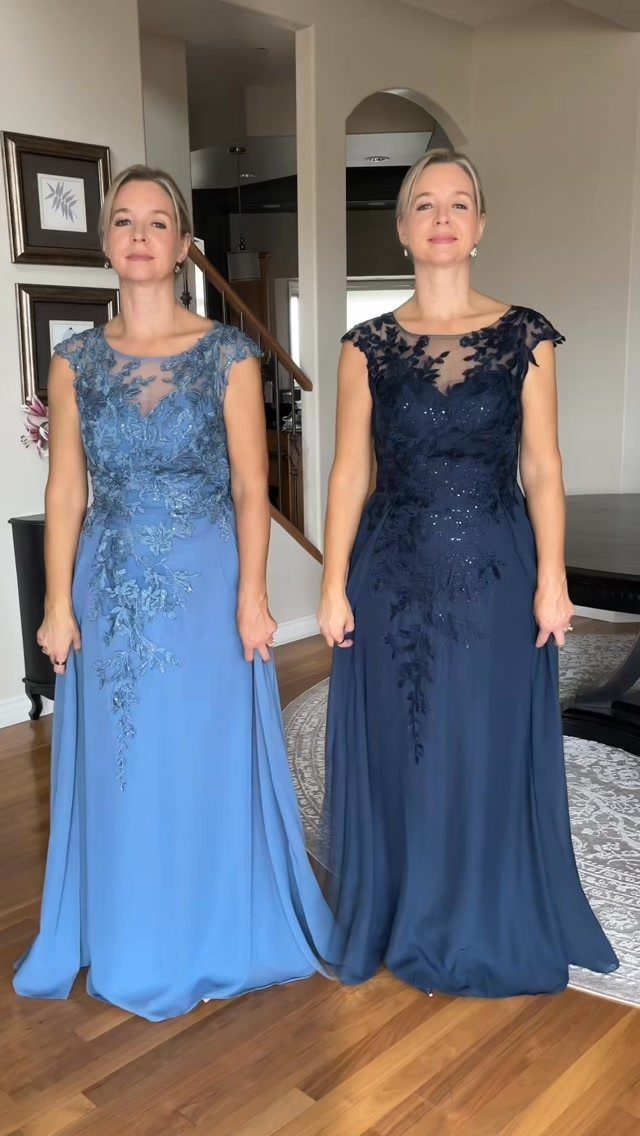 Two women posing in elegant, floor-length lace-detailed evening gowns in light blue and navy.