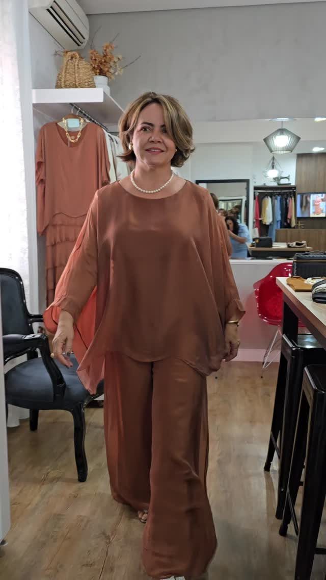 Middle-aged woman posing in a flowing burnt orange tunic and wide-leg trousers outfit.