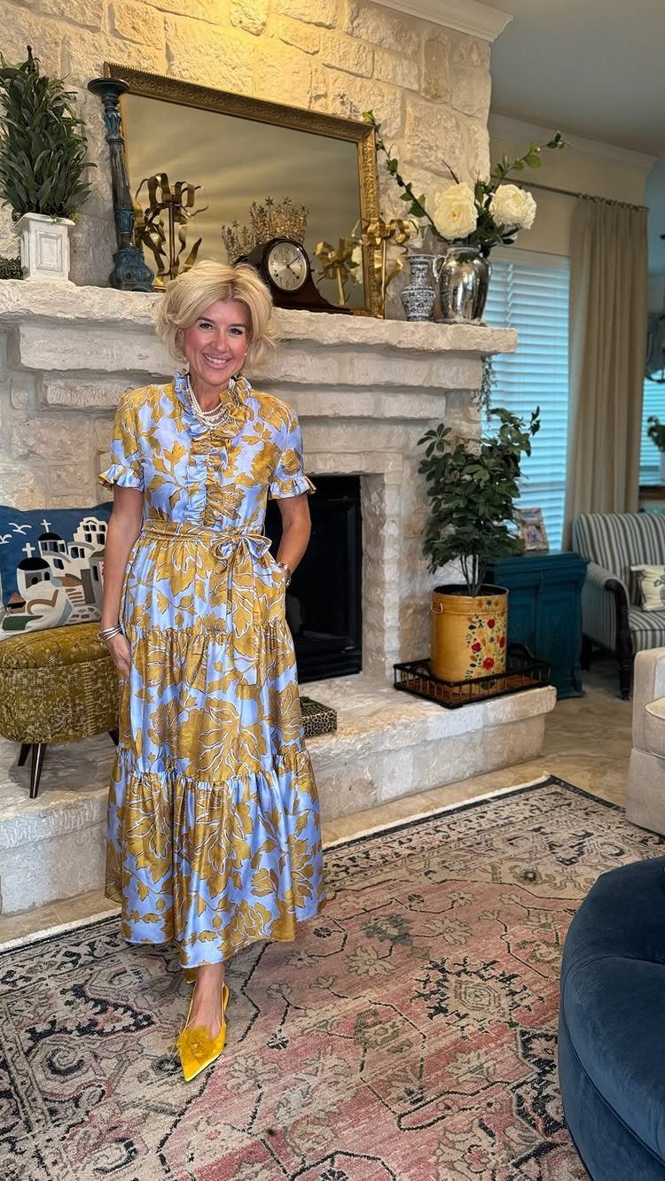 A blonde woman smiling while wearing a blue and gold patterned midi dress and yellow heels.