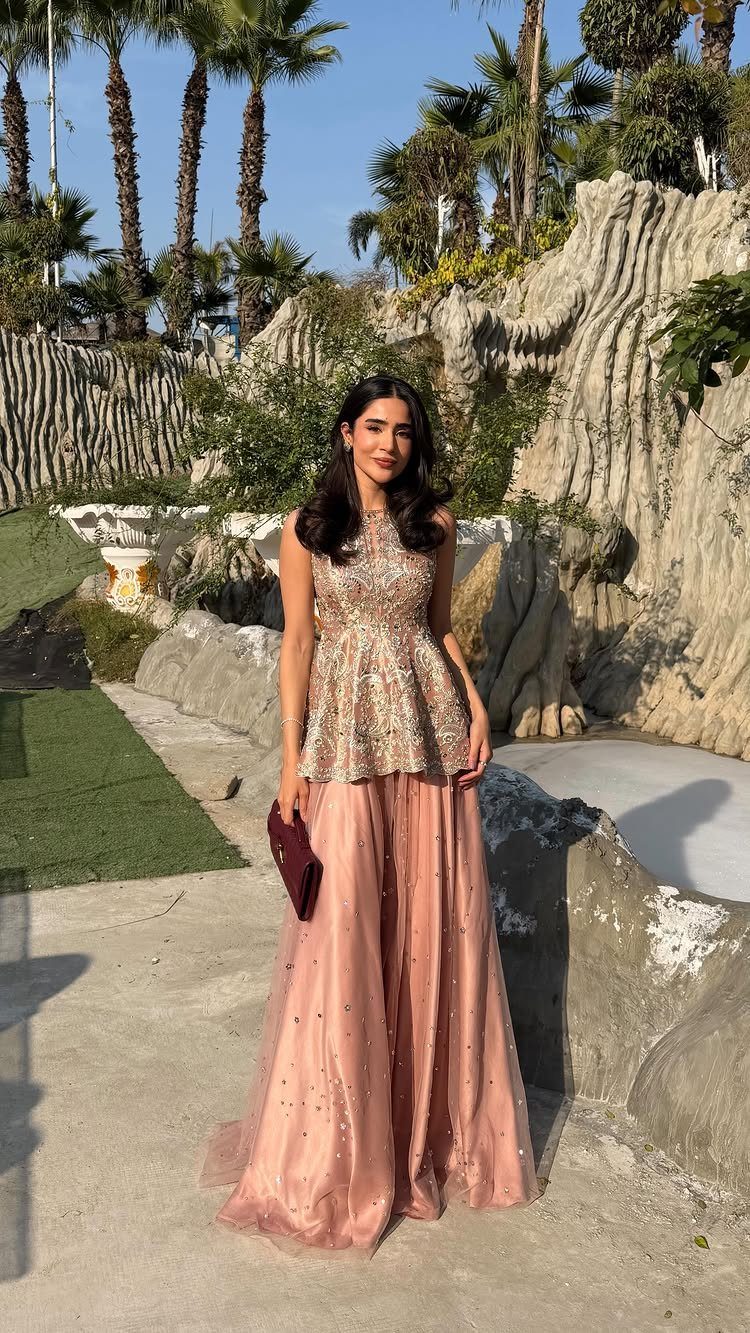 Woman in a peach embellished gown posing in front of palm trees and rocky terrain.