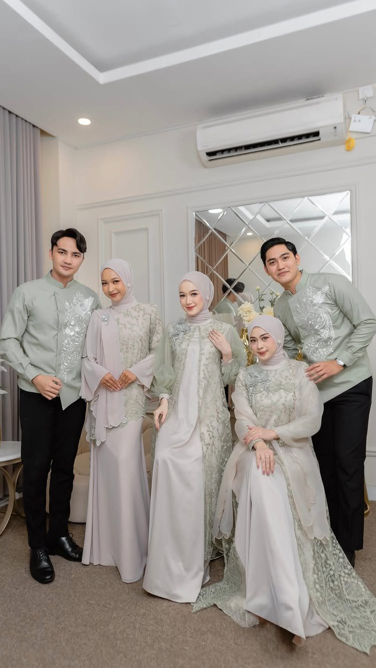 Five people in coordinated sage green formal attire posing together in a bright room.
