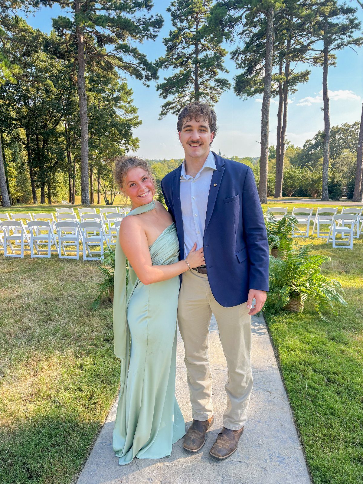 A woman in a mint green gown and a man in a navy blazer posing outdoors.
