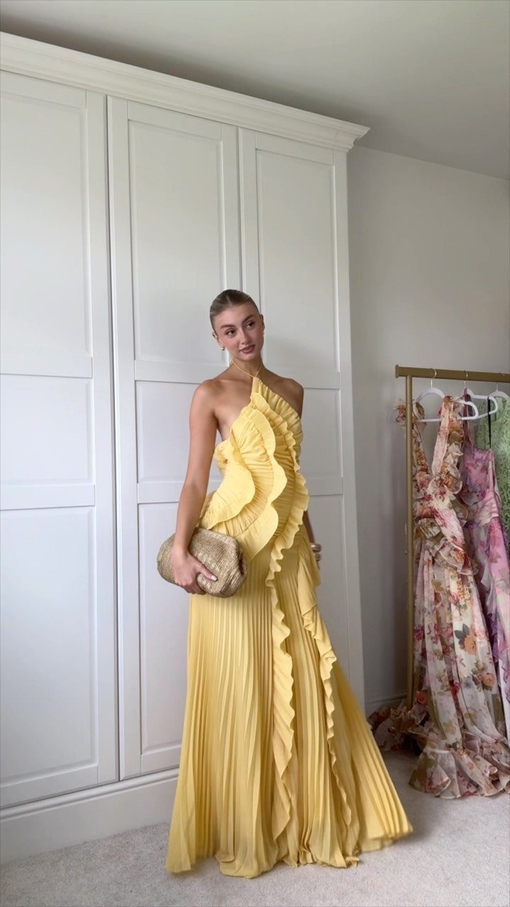Woman in a long yellow ruffled one-shoulder gown holding a gold clutch bag.