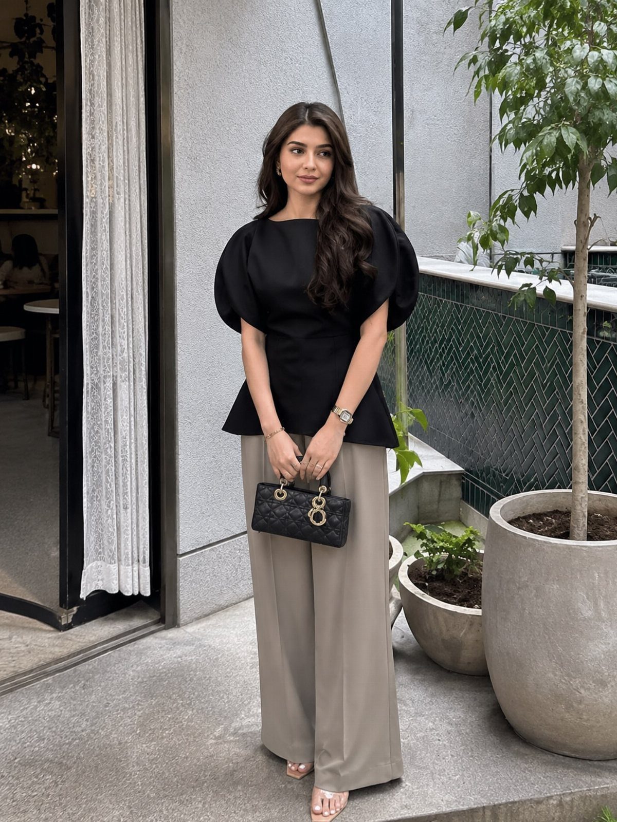 A woman posing in a black puff-sleeve blouse and wide-leg beige trousers.