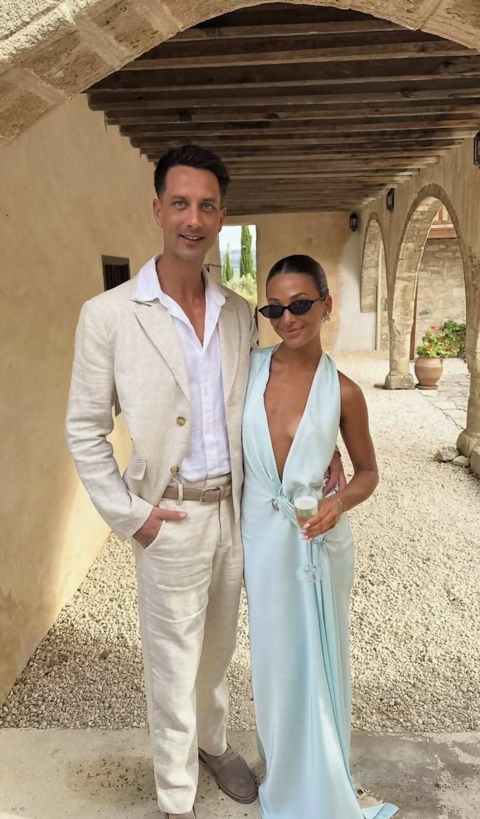 A man in a light beige linen suit and a woman in a light blue dress posing together.